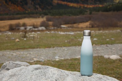 Thermo bottle on rock in mountains. Space for text