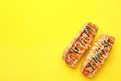 Delicious hot dogs with bacon, carrot and parsley on yellow background, top view. Space for text