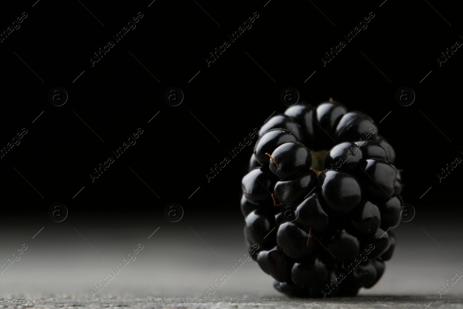 Photo of Tasty ripe blackberry on grey table against black background, closeup. Space for text