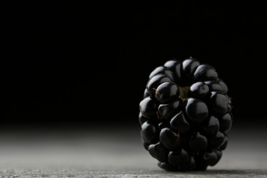 Photo of Tasty ripe blackberry on grey table against black background, closeup. Space for text