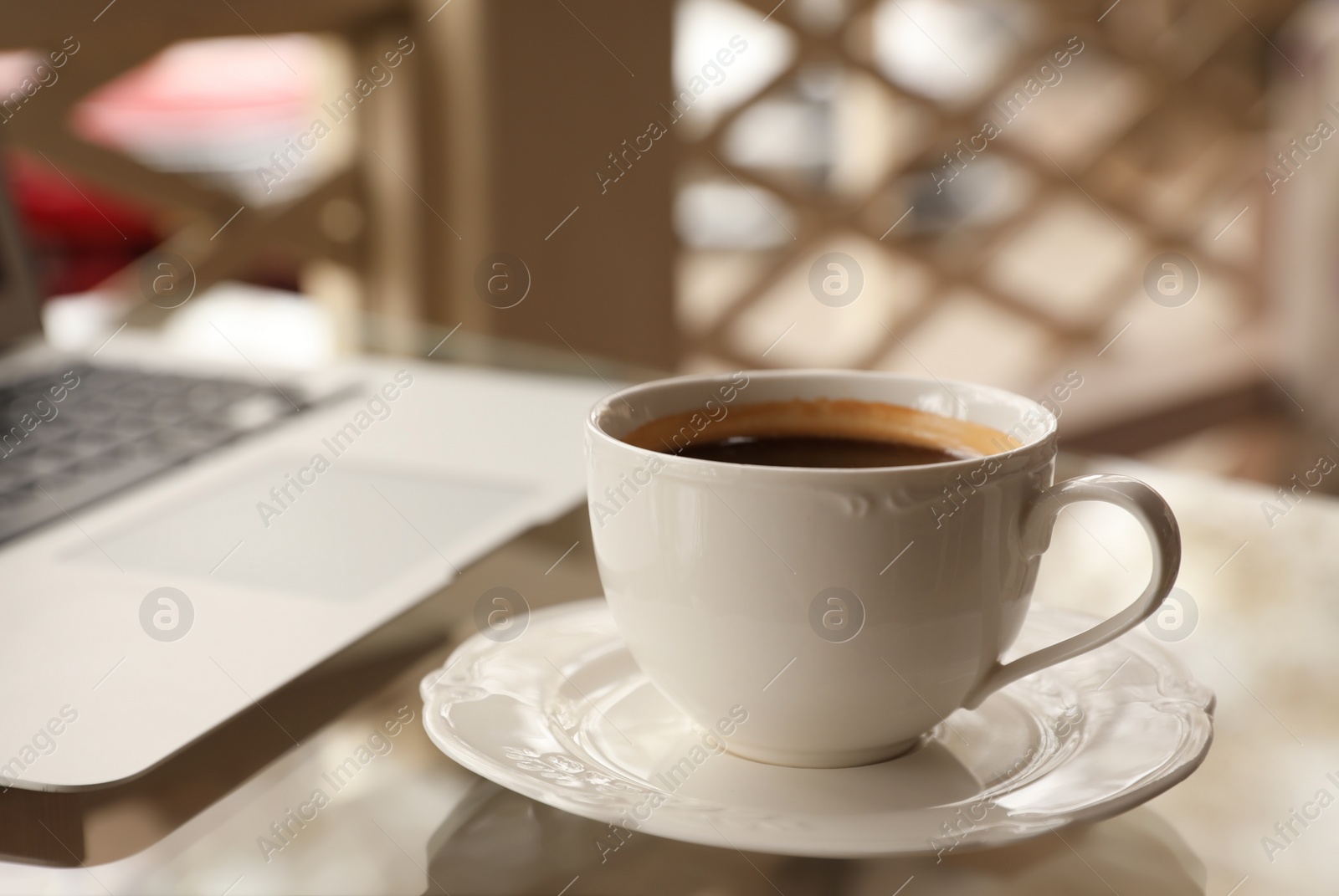 Photo of Cup of aromatic morning coffee and laptop on table in cafe