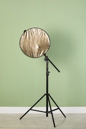Photo of Studio reflector on tripod near pale green wall indoors. Professional photographer's equipment