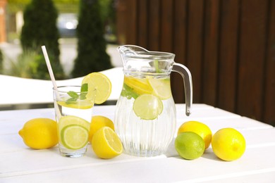 Water with lemons and limes on white wooden table outdoors