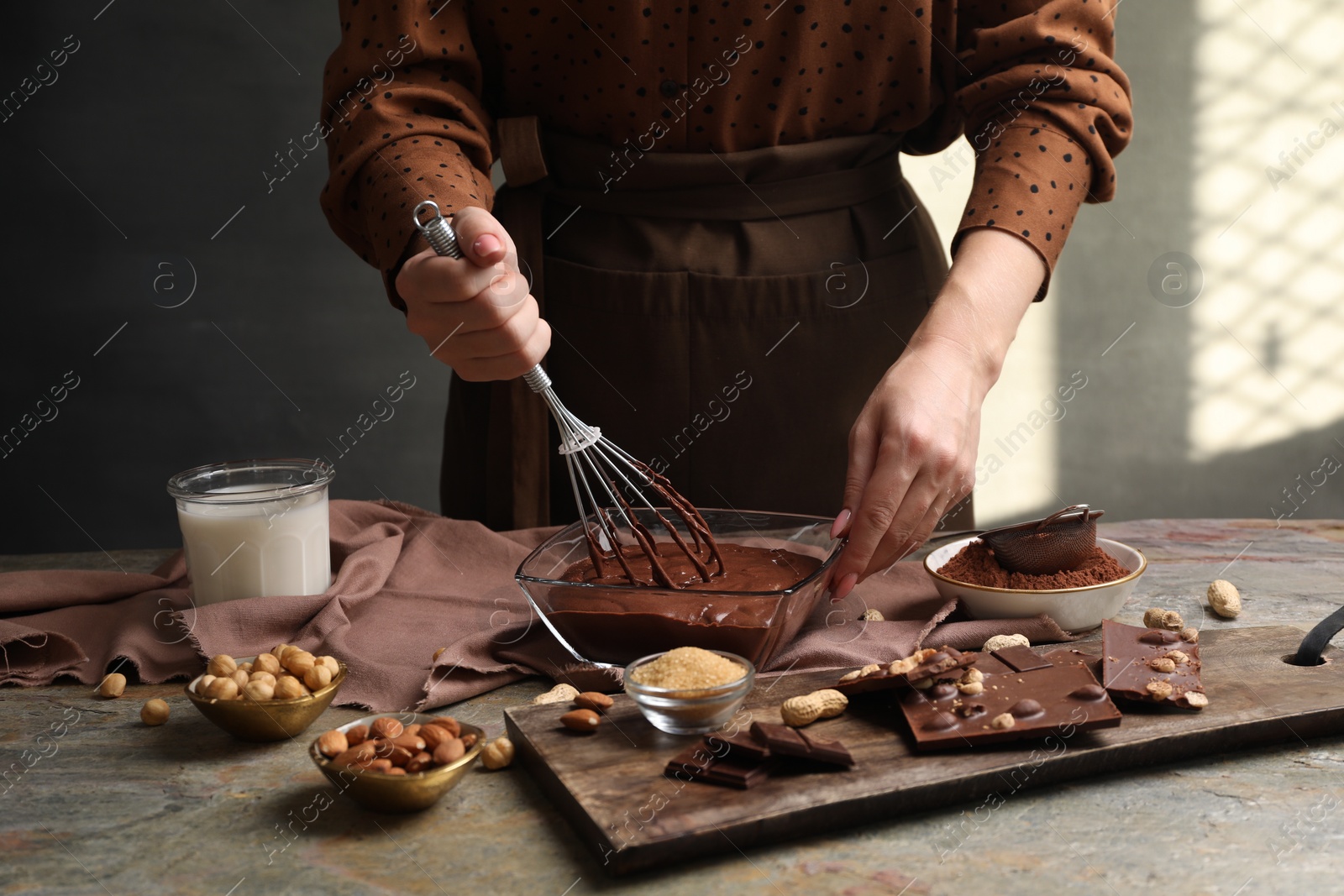 Photo of Woman mixing delicious chocolate cream with whisk at grey textured table, closeup