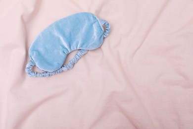 Photo of Light blue sleep mask on beige cloth, top view. Space for text