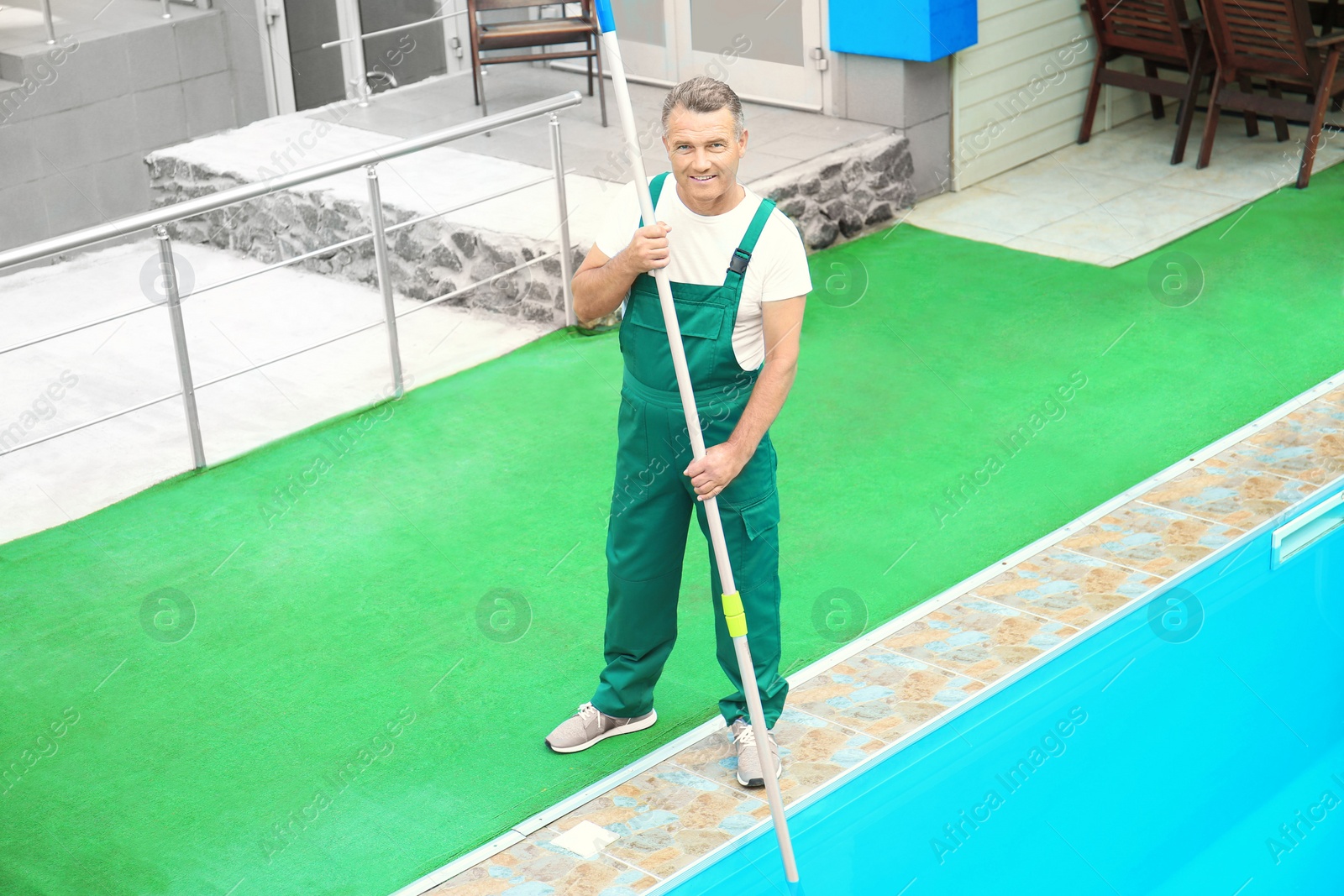 Photo of Male worker cleaning outdoor pool with underwater vacuum