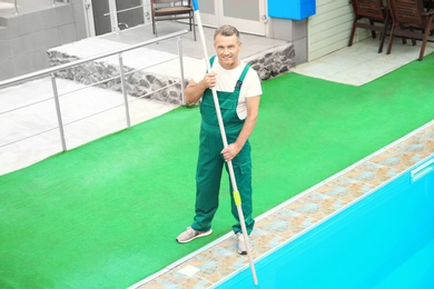 Photo of Male worker cleaning outdoor pool with underwater vacuum