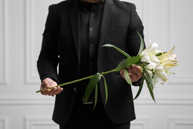 Photo of Man with lily flowers near white wall, closeup. Funeral ceremony