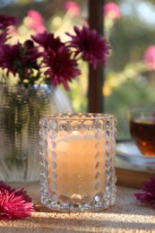 Burning scented candle in glass holder and chrysanthemum flowers on beige textured table. Autumn season
