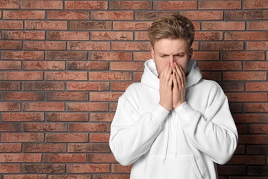 Photo of Handsome young man coughing near brick wall. Space for text