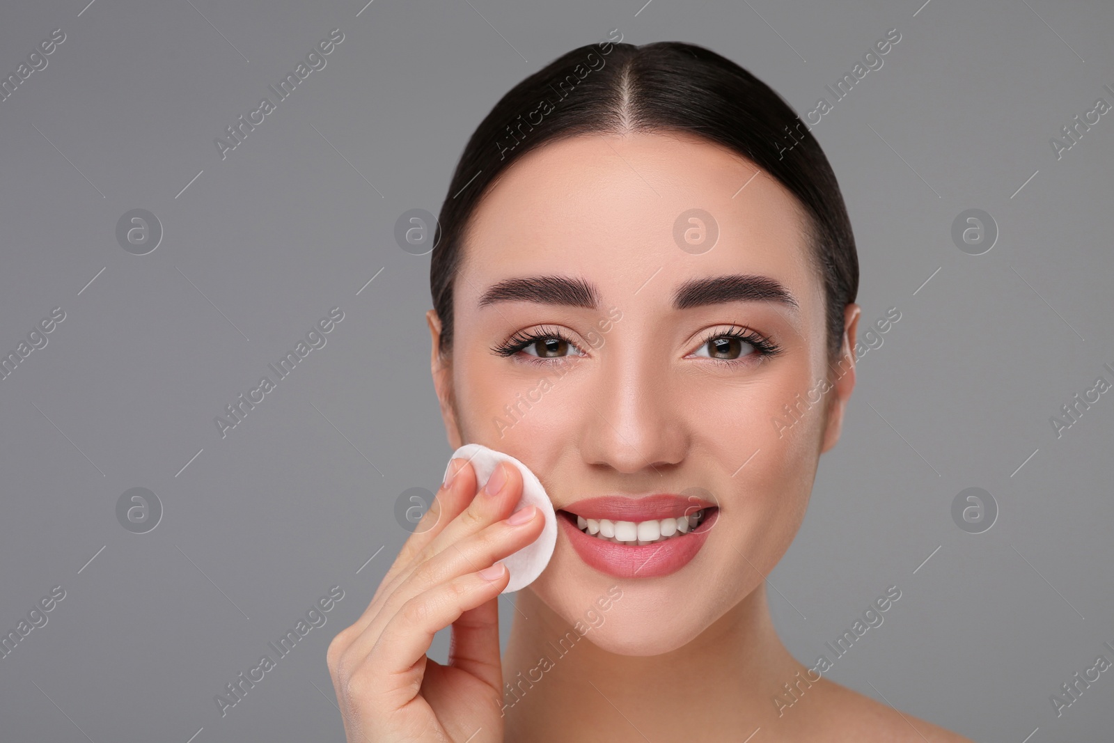 Photo of Beautiful woman removing makeup with cotton pad on gray background, space for text