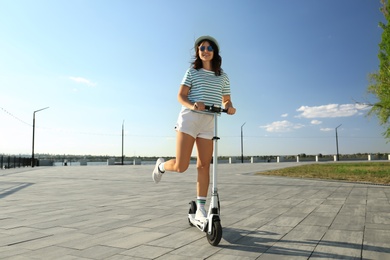 Photo of Young woman riding kick scooter along city street