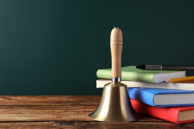 Photo of Golden bell, books and stationery on wooden table near green chalkboard, space for text. School days