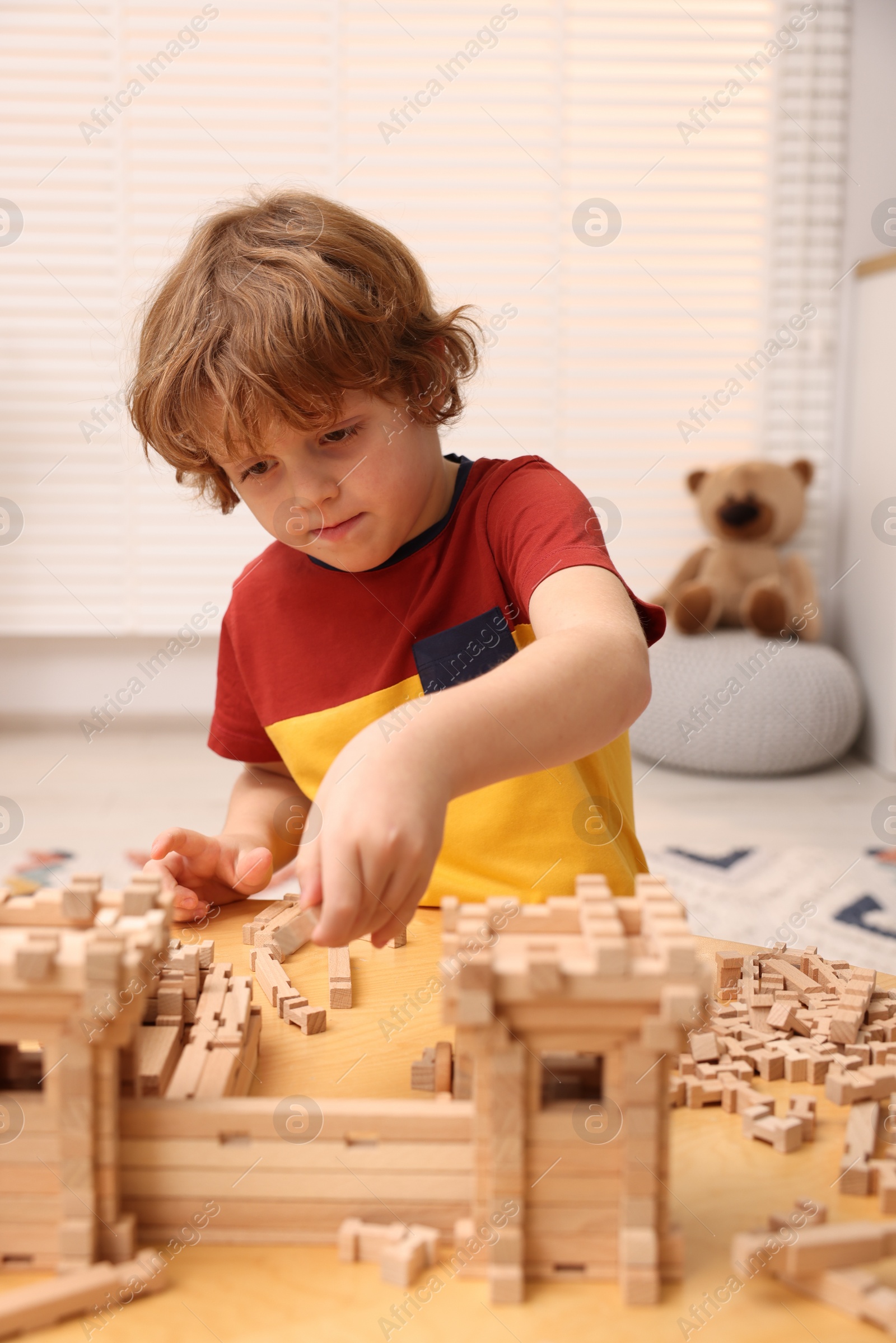 Photo of Little boy playing with wooden entry gate at table in room. Child's toy