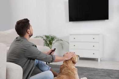 Photo of Man turning on TV near his cute Labrador Retriever at home, back view