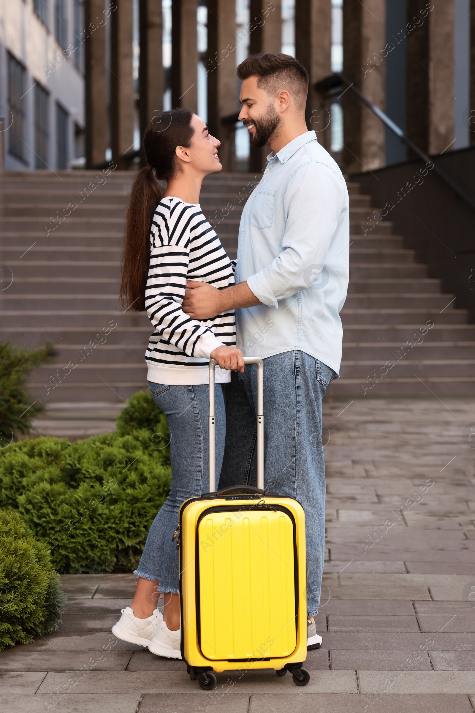 Photo of Long-distance relationship. Beautiful young couple with suitcase near building outdoors