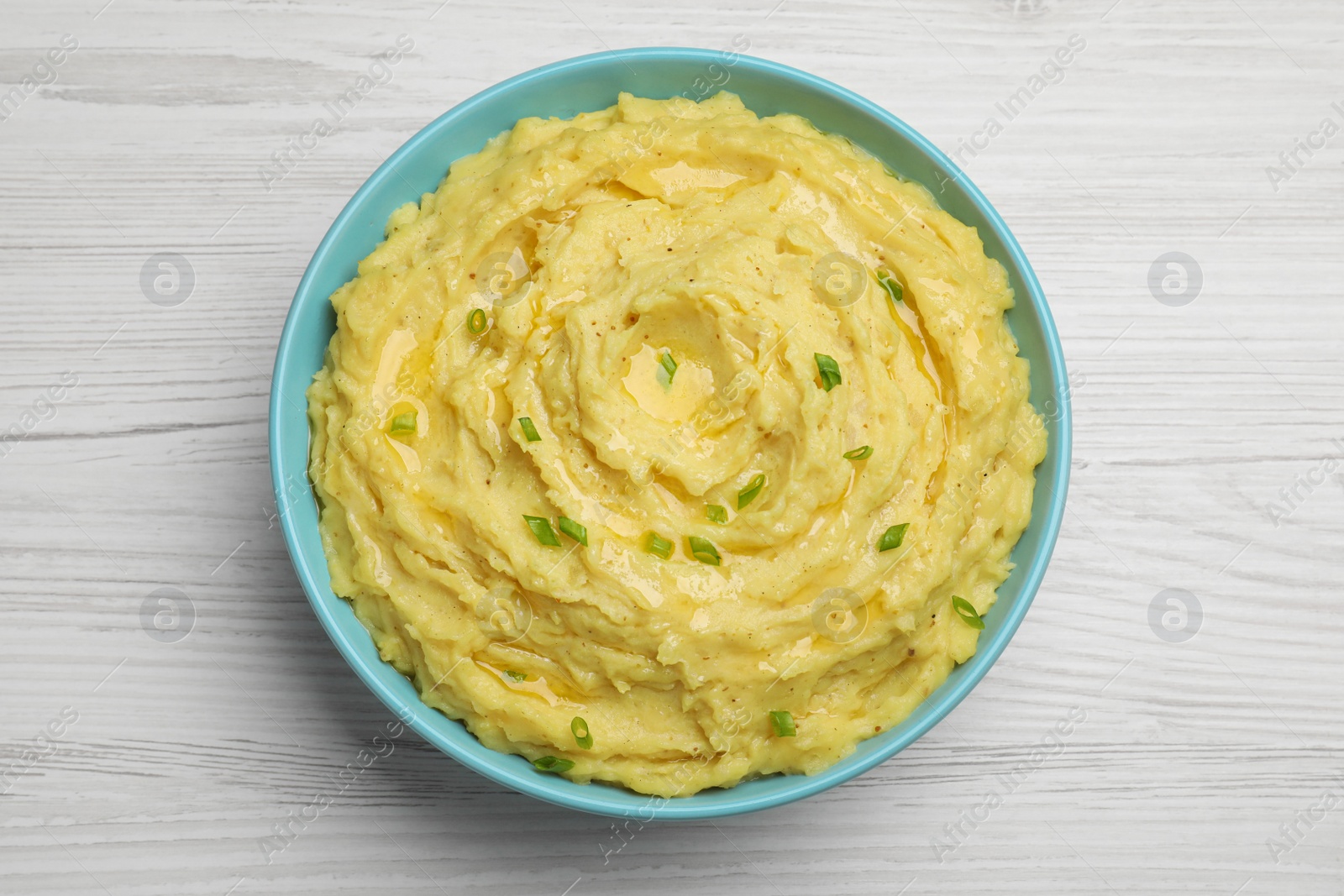 Photo of Bowl of tasty mashed potatoes with onion on white wooden table, top view