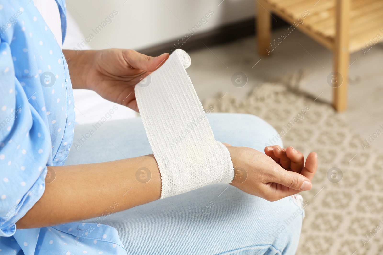 Photo of Young woman applying medical bandage onto wrist at home, closeup