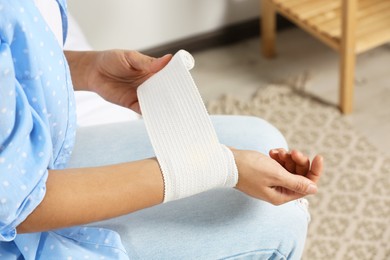 Photo of Young woman applying medical bandage onto wrist at home, closeup