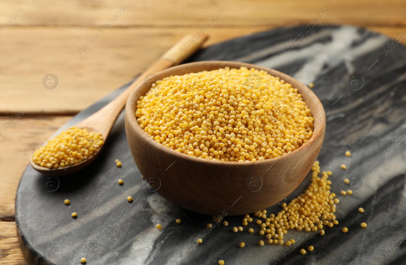 Photo of Millet groats in bowl and spoon on wooden table