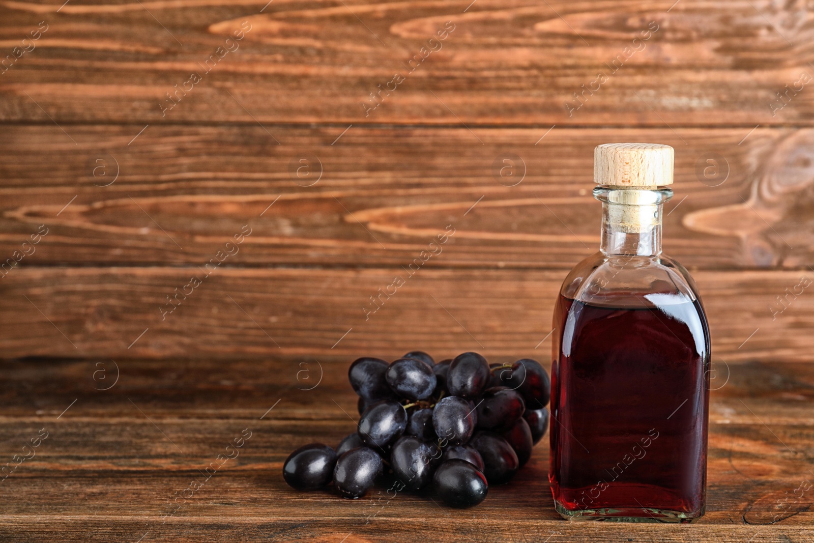 Photo of Bottle with wine vinegar and fresh grapes on wooden table. Space for text