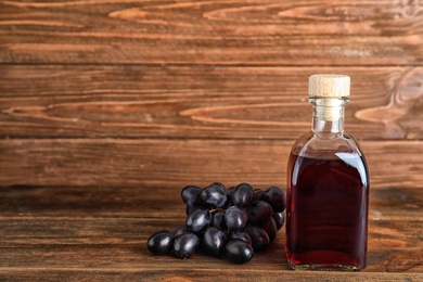 Bottle with wine vinegar and fresh grapes on wooden table. Space for text