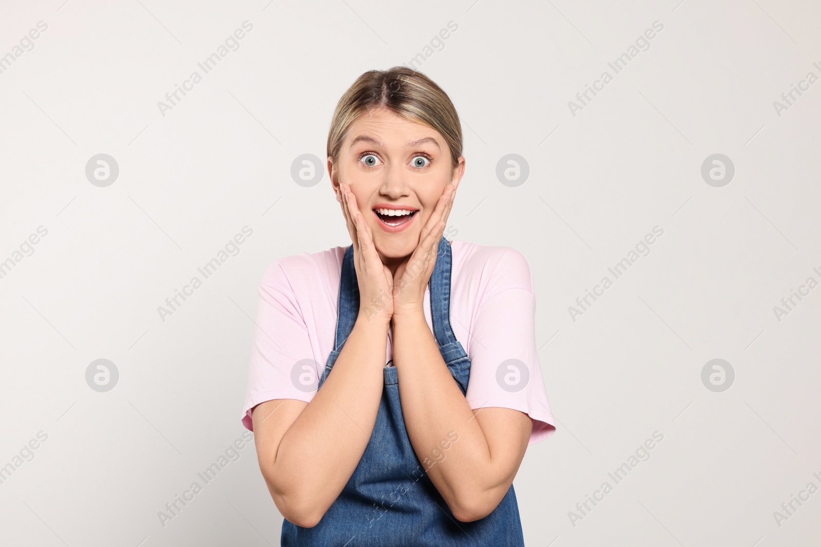 Photo of Beautiful young woman in denim apron on light grey background