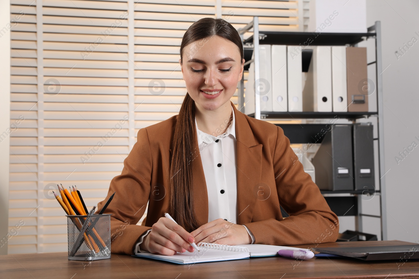 Photo of Happy woman taking notes at wooden table in office