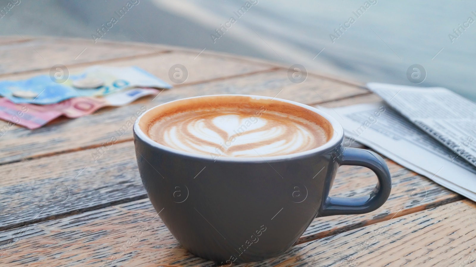 Photo of Cup of delicious coffee, newspaper and banknotes on wooden table, closeup