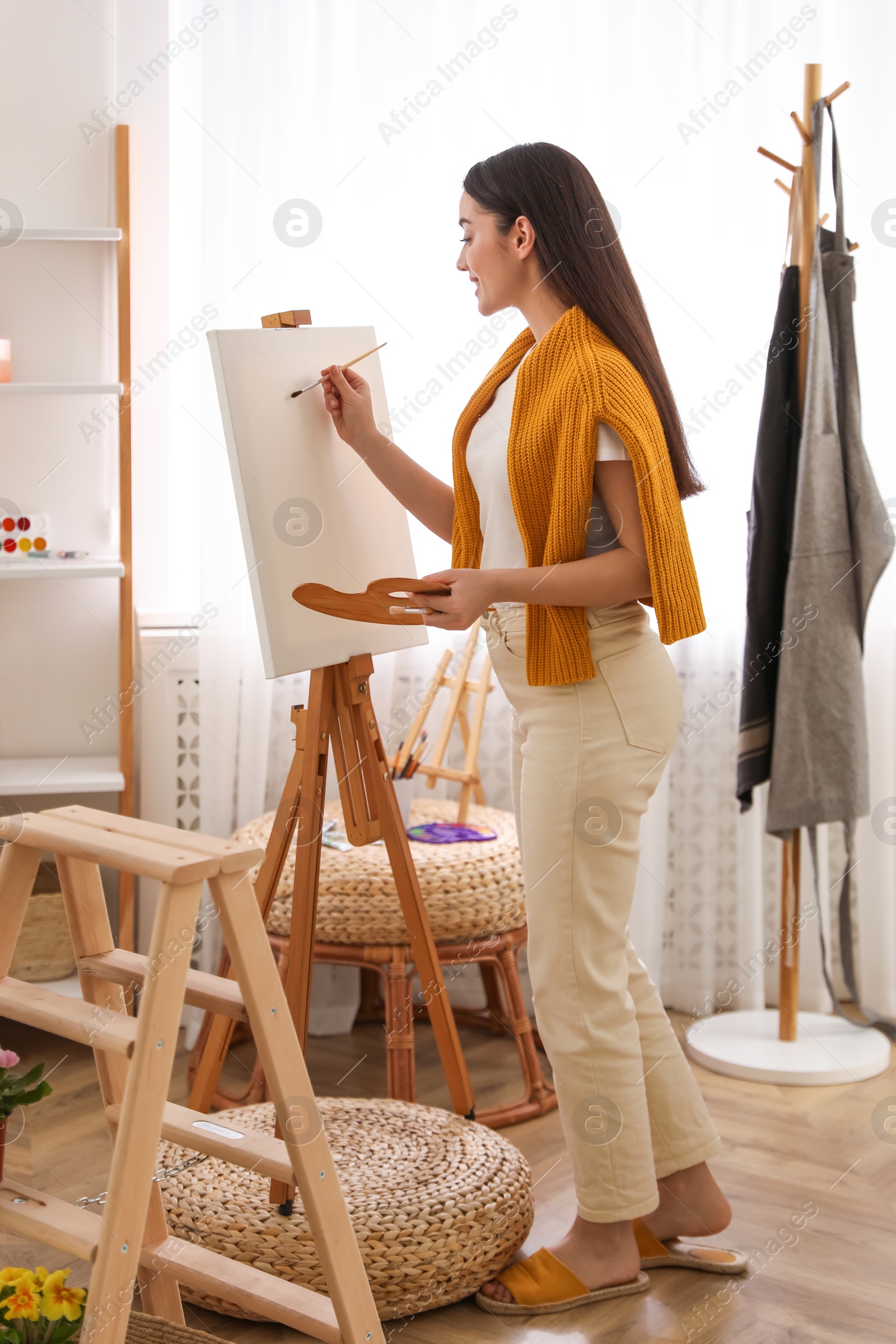 Photo of Beautiful young woman drawing on easel at home