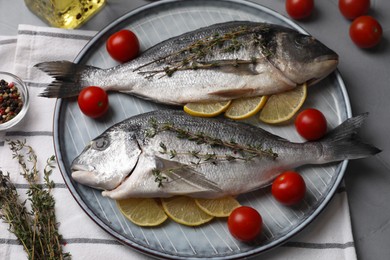 Photo of Raw dorado fish with thyme, lemon slices and tomatoes on table, closeup