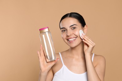 Photo of Young woman using cotton pad with micellar water on beige background