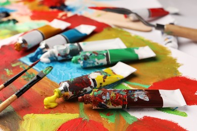 Photo of Tubes of colorful oil paints and brushes on canvas with abstract painting, closeup