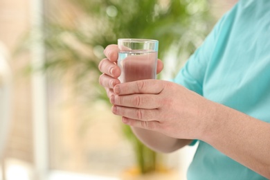 Closeup view of elderly man with glass of water in nursing home, space for text. Assisting senior generation