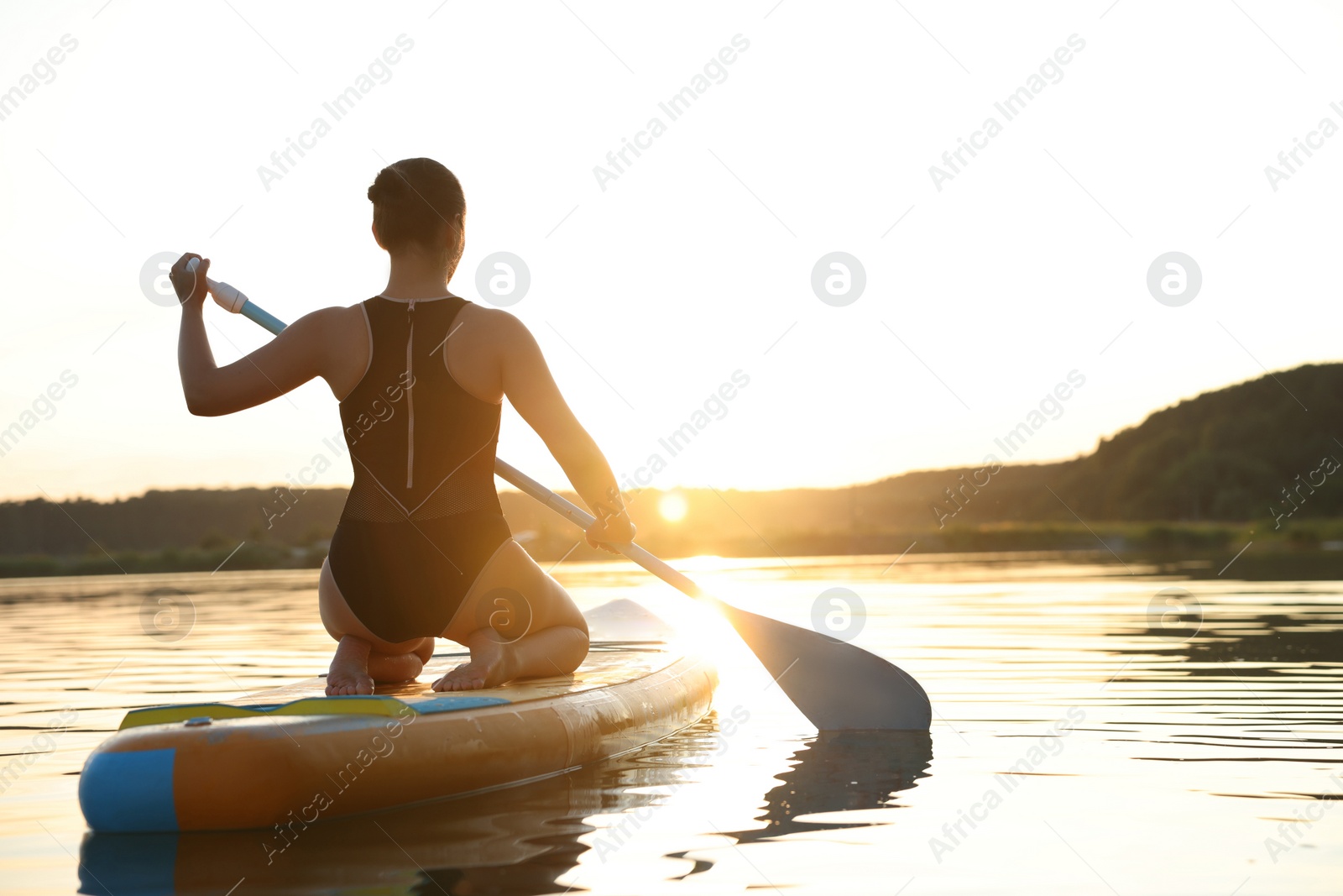 Photo of Woman paddle boarding on SUP board in river at sunset, back view