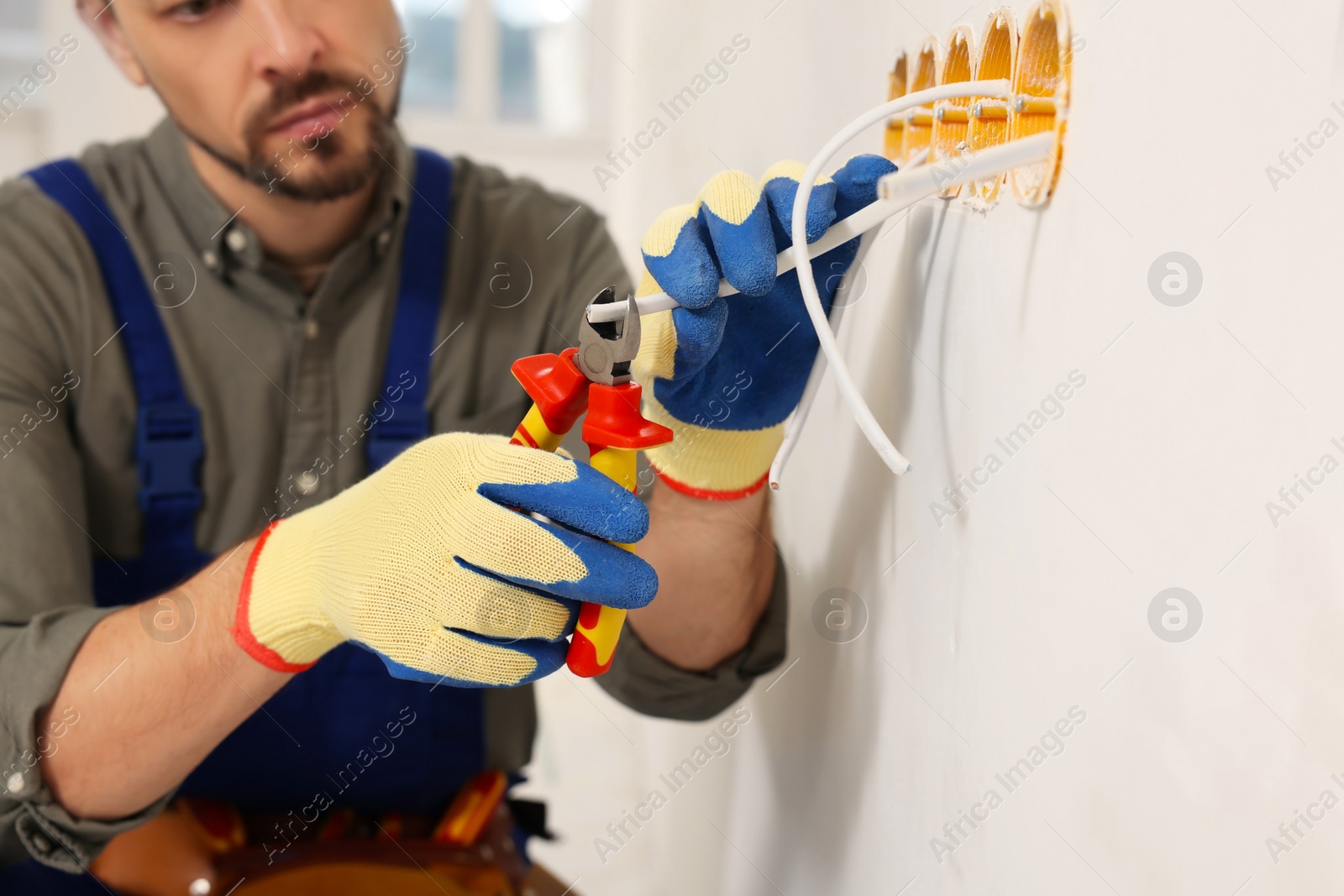 Photo of Electrician with pliers repairing power socket indoors, closeup