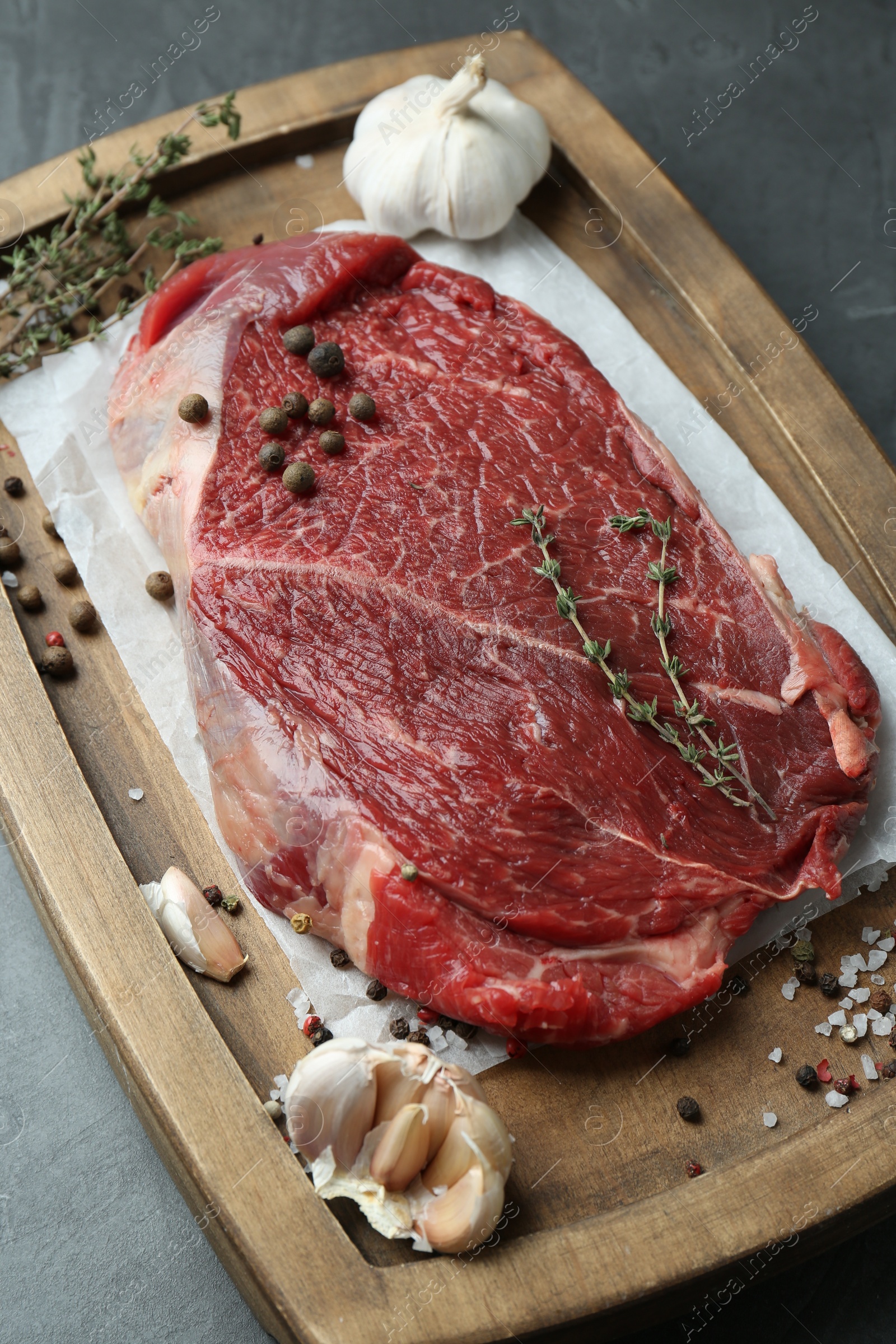 Photo of Wooden tray with piece of raw meat, garlic and thyme on grey table