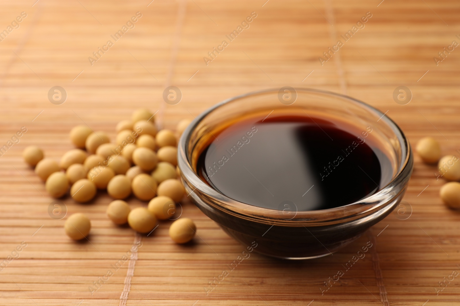 Photo of Soy sauce in bowl and soybeans on bamboo mat, closeup