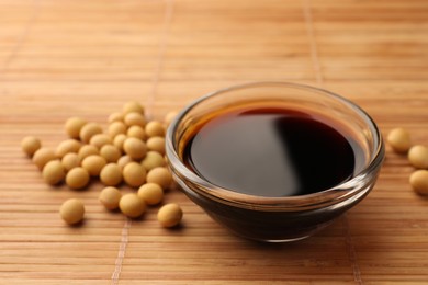 Soy sauce in bowl and soybeans on bamboo mat, closeup