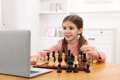 Cute girl learning to play chess with online tutor at home