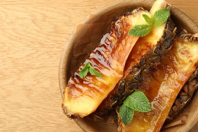 Tasty grilled pineapples in bowl on wooden table, top view. Space for text