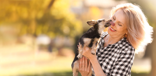 Image of Beautiful mature woman with her cute pet in park, space for text. Banner design