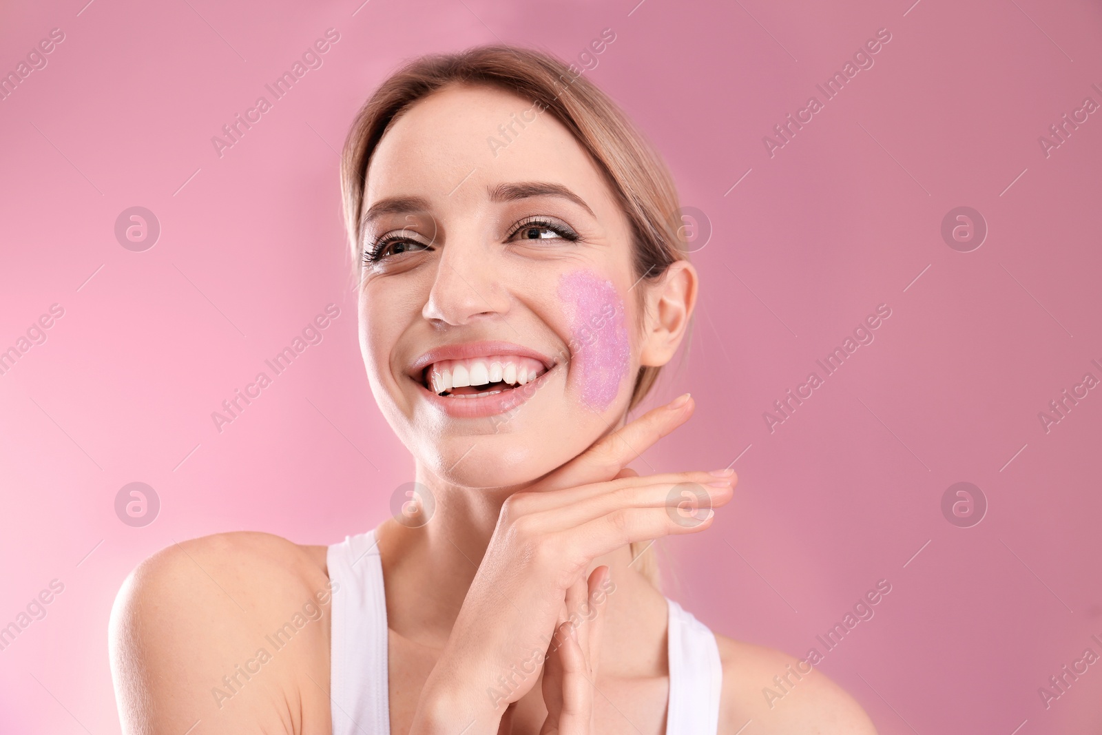 Photo of Young woman applying natural scrub on her face against color background