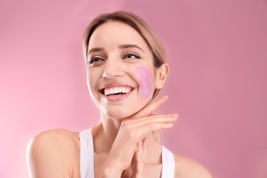 Young woman applying natural scrub on her face against color background