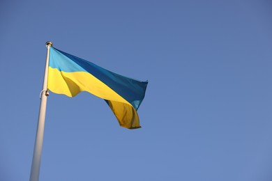 Photo of Flag of Ukraine fluttering against blue sky, low angle view. Space for text