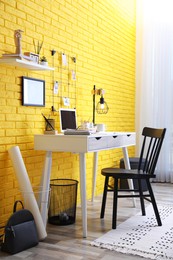 Stylish home office interior with comfortable workplace near yellow brick wall