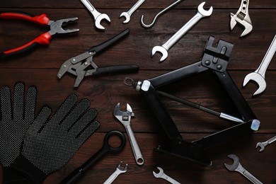 Photo of Car scissor jack, gloves and different tools on wooden surface, flat lay