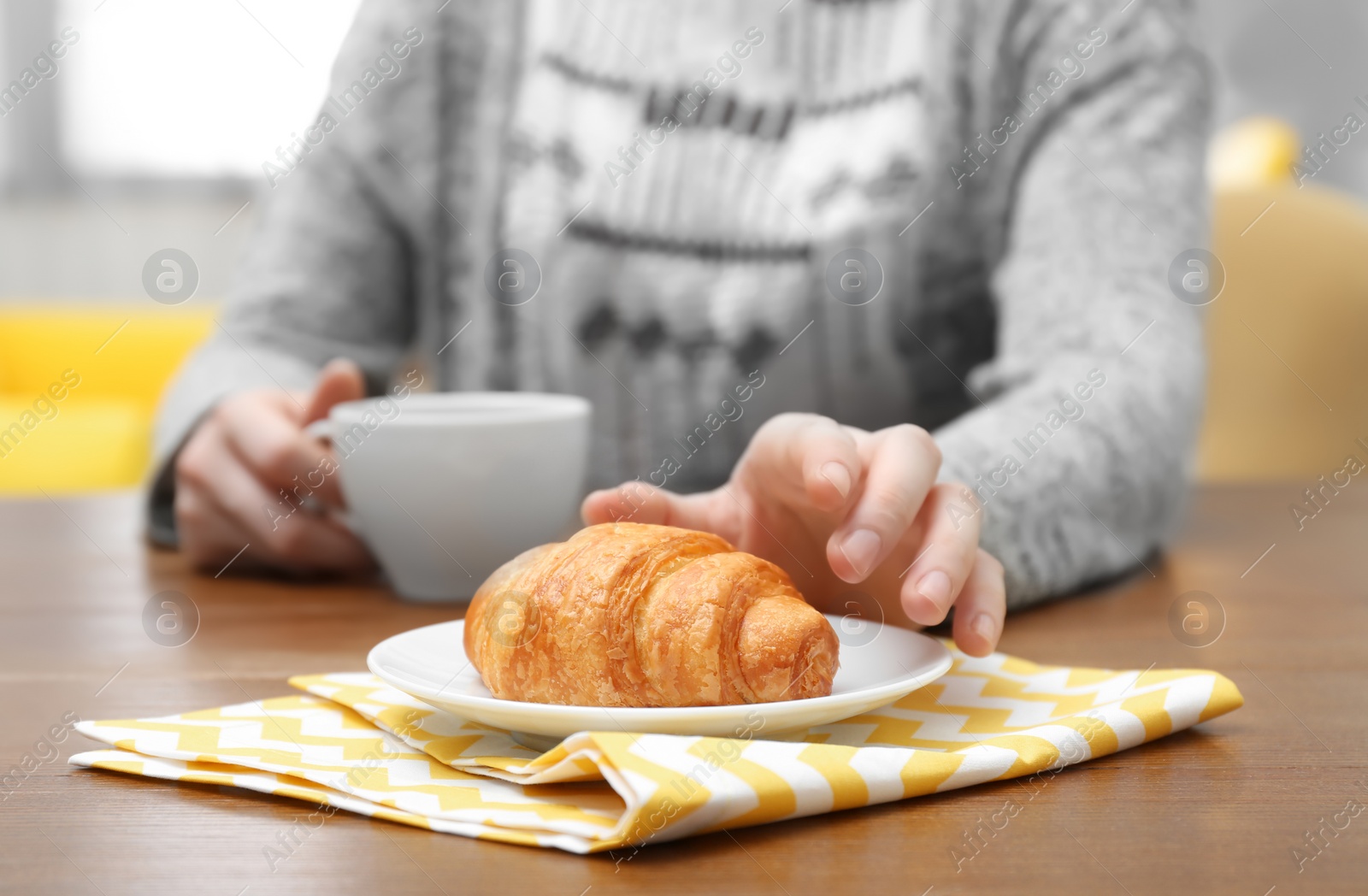 Photo of Young woman having breakfast with tasty croissant and cup of coffee at table