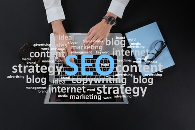 Image of Search engine optimization (SEO). Cloud of words above copywriter with laptop at black table, top view