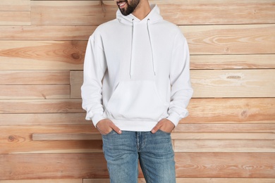 Young man in sweater at wooden wall, closeup. Mock up for design